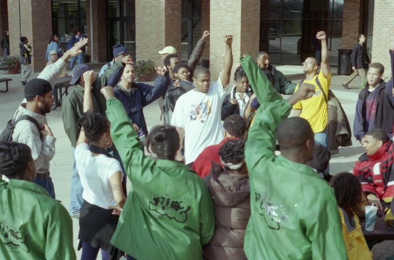 一群非洲裔美国人站在外面，他们的拳头在空中举起的彩色照片